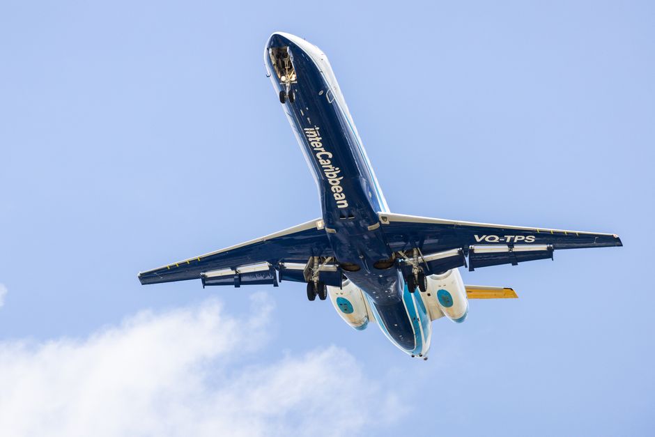 A view from an airplane window showing the airplane's wing with a yellow wingtip marked 'Boeing' extending into a sky filled with scattered white clouds below. The wing surface is smooth and metallic,