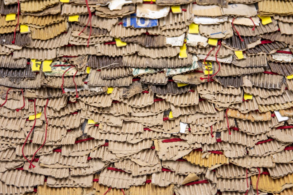 A collection of flattened and crumpled cardboard boxes and paper-based packaging materials piled inside a designated recycling area. The cardboard appears in various shades of brown, with some section